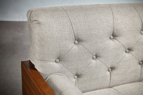 Close-up of a beige tufted fabric club chair with wooden armrest.